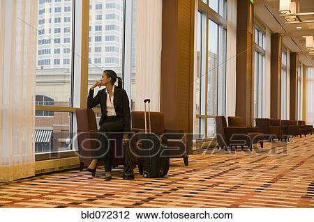 Stock Image - African businesswoman with suitcase looking out window. Fotosearch
