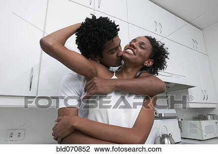 Stock Image - African couple hugging in kitchen. Fotosearch