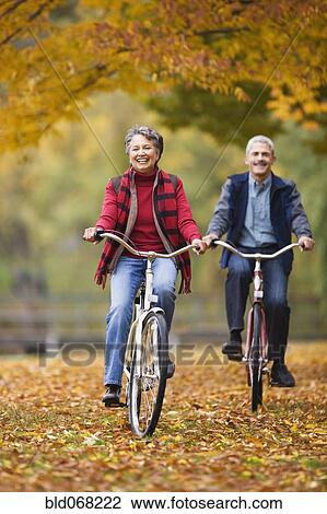 Stock Image - African couple riding bicycles in park in autumn. Fotosearch