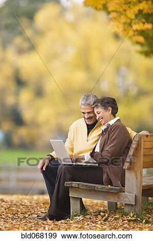 Stock Photo - African couple using laptop on park bench in autumn. Fotosearch