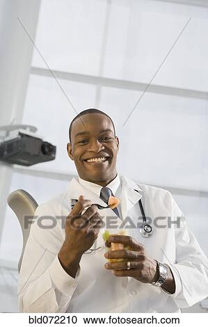 Stock Image - African doctor eating fruit. Fotosearch