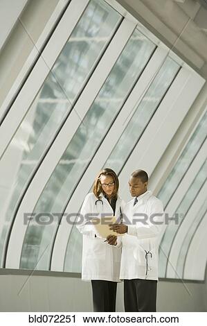 Stock Image - African doctors reviewing medical chart in corridor. Fotosearch