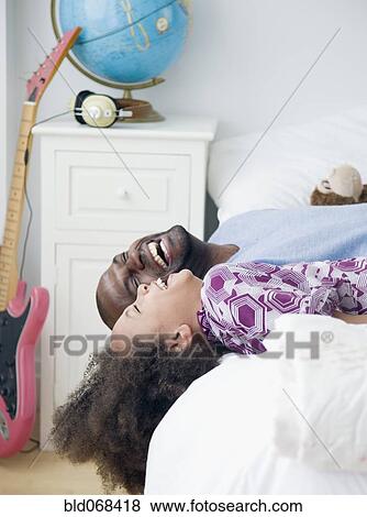 Stock Photo - African father and daughter laughing on bed. Fotosearch