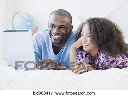 African father and daughter using laptop on bed View Large Photo Image Stock Photo - African father and daughter using laptop on bed. Fotosearch