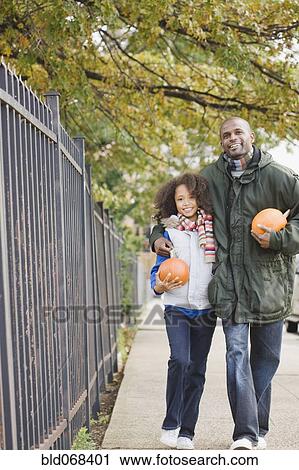 Stock Image - African father and daughter walking with pumpkins. Fotosearch