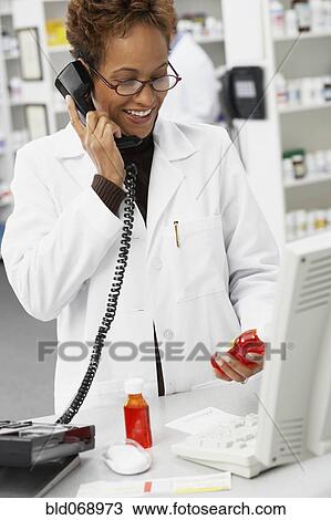 Stock Image - African female pharmacist talking on telephone. Fotosearch