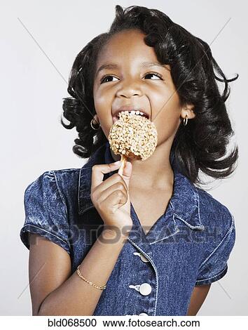 Stock Image - African girl eating candy apple. Fotosearch