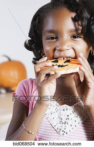 Picture - African girl eating Halloween cookie. Fotosearch