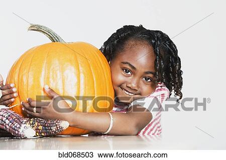 Stock Image - African girl hugging pumpkin. Fotosearch