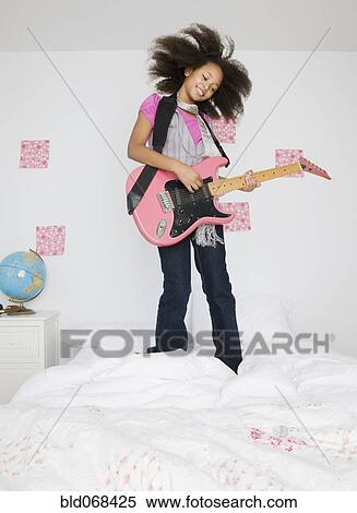 Stock Photography - African girl playing guitar on bed. Fotosearch
