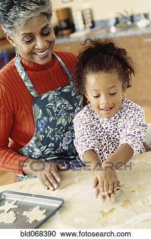 Stock Image - African grandmother and granddaughter making cookies. Fotosearch