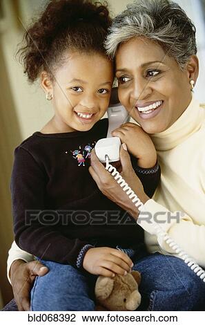 Stock Image - African grandmother and granddaughter using telephone. Fotosearch