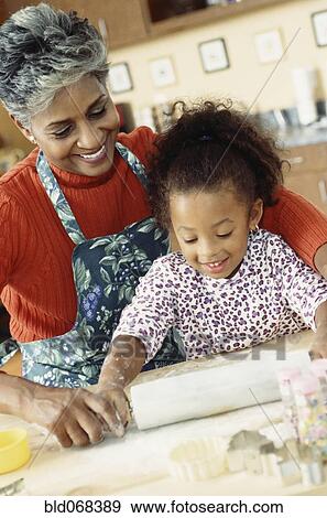 Stock Photo - African grandmother and granddaughter rolling dough. Fotosearch