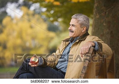 Stock Photo - African man eating apple on park bench. Fotosearch