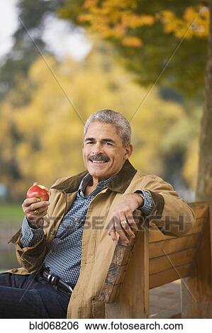 Stock Photograph - African man eating apple on park bench. Fotosearch