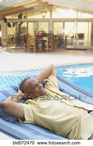 Stock Image - African man laying in hammock at poolside. Fotosearch