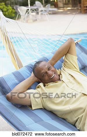 Stock Image - African man laying in hammock at poolside. Fotosearch