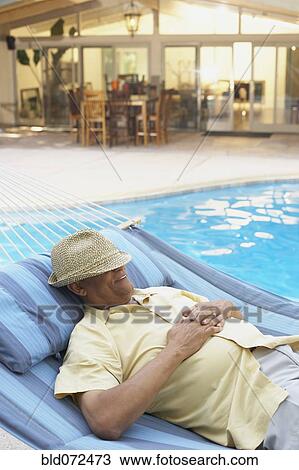 Stock Image - African man sleeping in hammock at poolside. Fotosearch