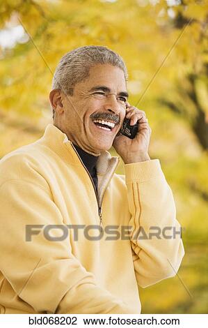 Stock Image - African man using cell phone outdoors in autumn. Fotosearch