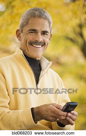 Stock Image - African man using cell phone outdoors in autumn. Fotosearch