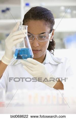 Stock Image - African scientist holding beaker of liquid in laboratory. Fotosearch