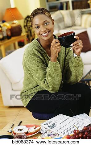 Picture - African woman drinking coffee in livingroom. Fotosearch