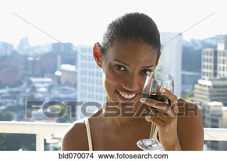 Picture - African woman drinking wine on balcony. Fotosearch