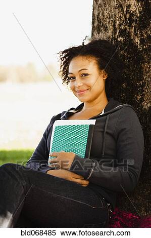 African woman holding book leaning against tree View Large Photo Image Stock Photography - African woman holding book leaning against tree. Fotosearch