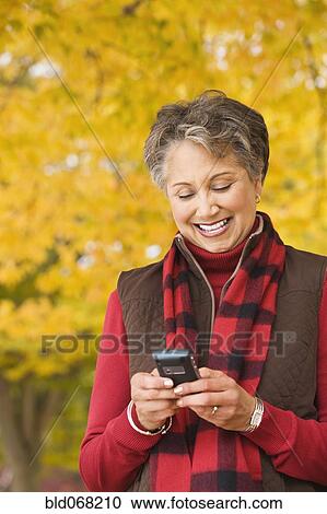 Stock Image - African woman holding cell phone outdoors in autumn. Fotosearch