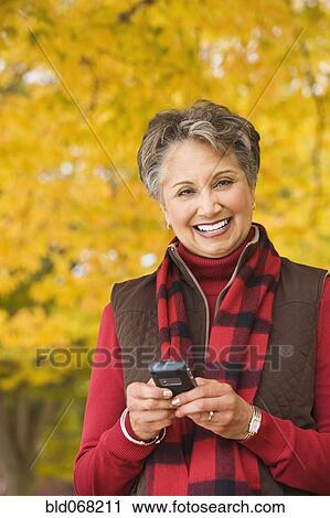 Stock Image - African woman holding cell phone outdoors in autumn. Fotosearch