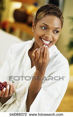 Stock Image - African woman in bathrobe eating grape. Fotosearch