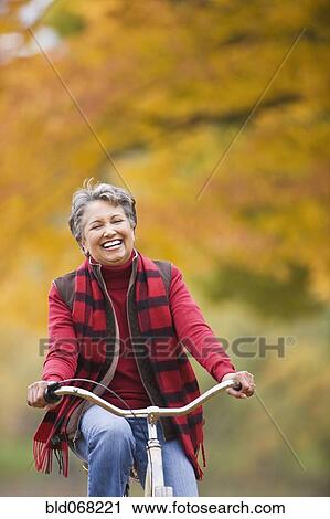 Stock Image - African woman riding bicycle in park in autumn. Fotosearch