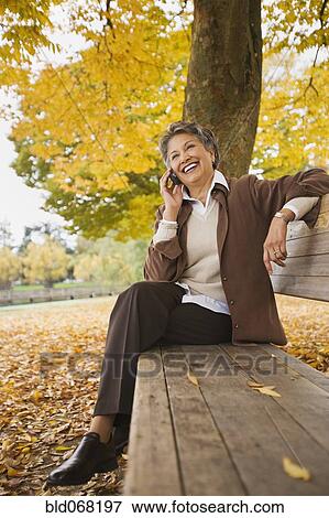 Stock Photo - African woman talking on cell phone on park bench in autumn. Fotosearch