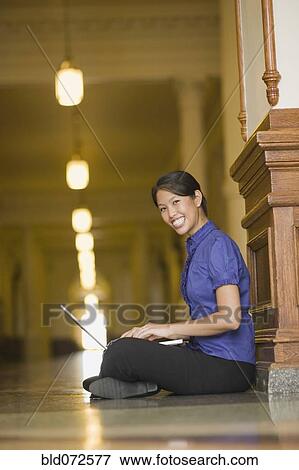 Stock Photo - African woman typing on laptop in corridor. Fotosearch