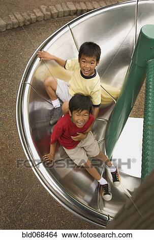 Picture - Asian boys sliding down circular slide. Fotosearch