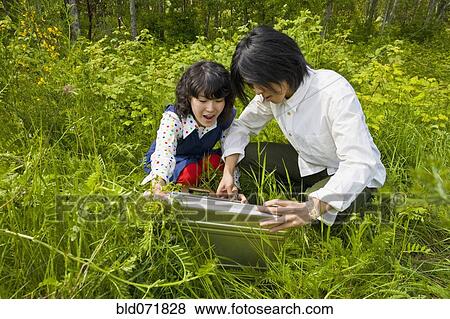 Stock Photo - Asian couple opening briefcase in tall grass. Fotosearch