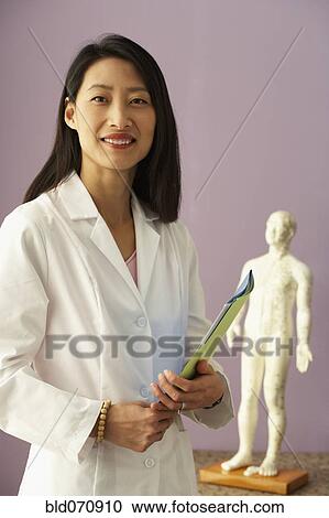 Stock Image - Asian female doctor next to Acupuncture model. Fotosearch