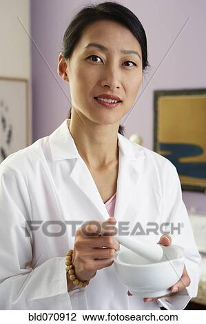 Stock Image - Asian female doctor using mortal and pestle. Fotosearch