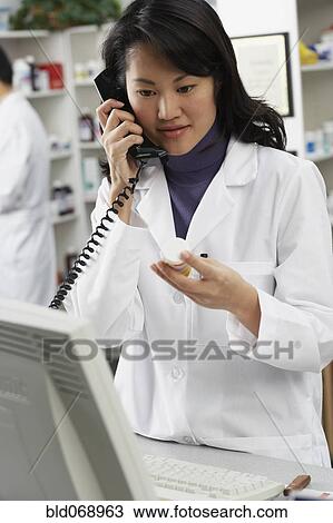 Stock Image - Asian female pharmacist talking on telephone. Fotosearch