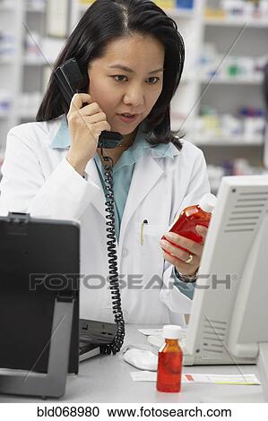 Stock Image - Asian female pharmacist talking on telephone. Fotosearch