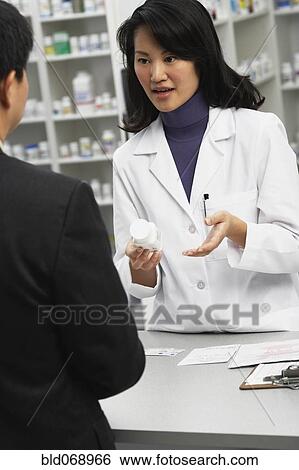 Stock Photograph - Asian female pharmacist talking to customer. Fotosearch