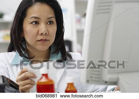 Stock Image - Asian female pharmacist working on computer. Fotosearch