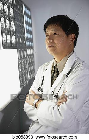 Stock Image - Asian male doctor looking at x-rays. Fotosearch