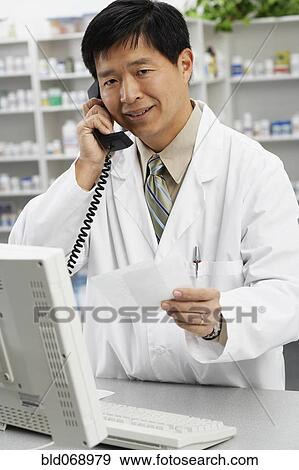 Stock Photo - Asian male pharmacist talking on telephone. Fotosearch