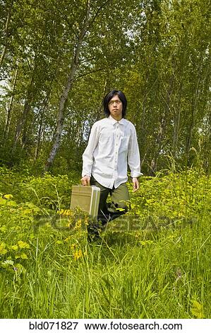 Stock Photo - Asian man carrying briefcase in tall grass. Fotosearch
