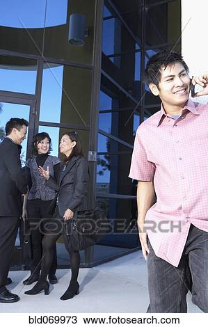 Stock Image - Asian man talking on cell phone next to businesspeople. Fotosearch