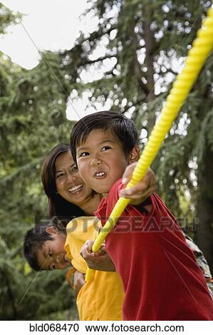 Stock Image - Asian mother and sons playing tug-of-war. Fotosearch