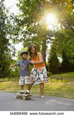Stock Photo - Asian mother helping son learn to skateboard. Fotosearch