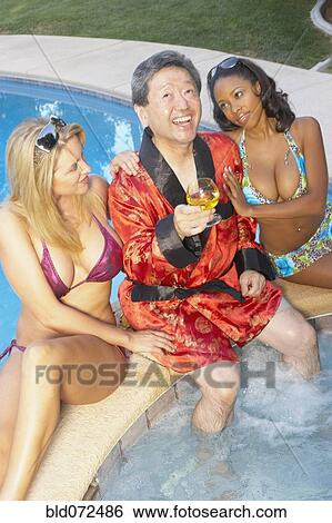 Stock Photograph - Asian playboy enjoying hot tub with young girlfriends. Fotosearch