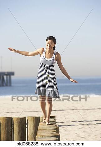 Stock Photography - Asian woman balancing on posts at beach. Fotosearch